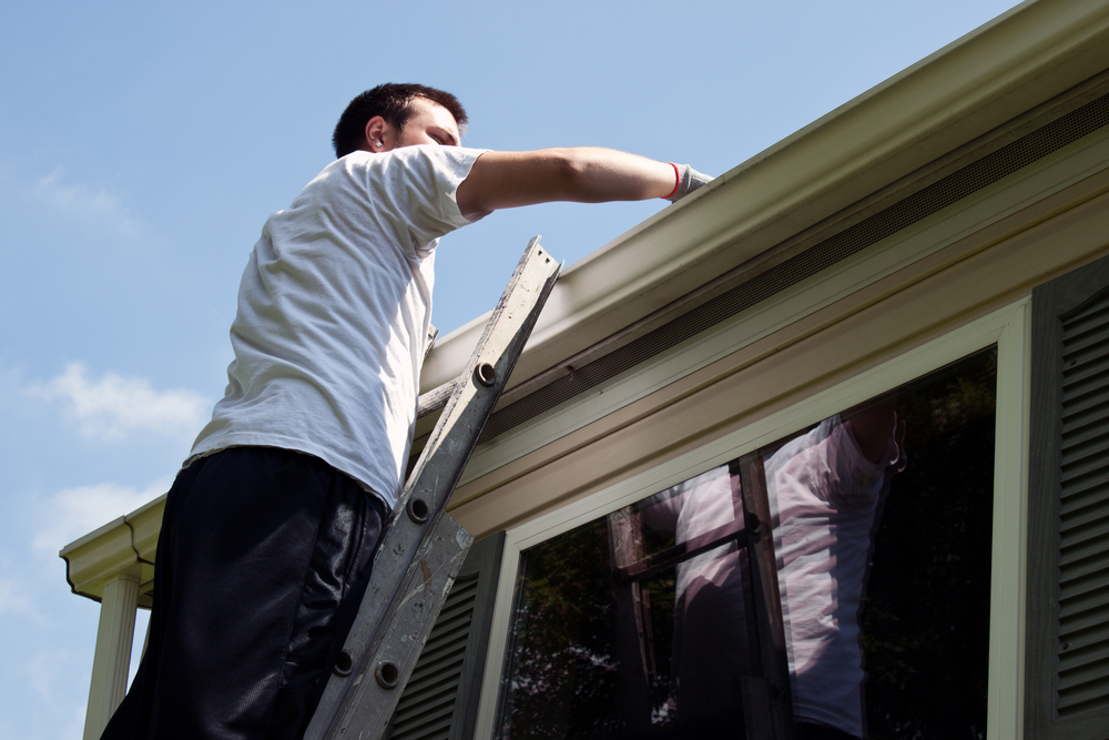 Man on ladder cleaning out gutters.